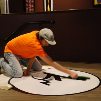Man applying white screen printed decal to floor