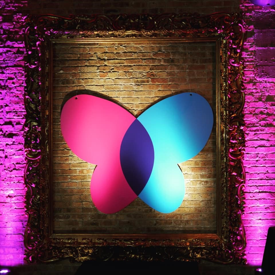 A custom event graphic of a multicolored butterfly hanging inside a gold picture frame