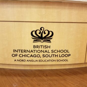 Black acrylic wall sign mounted on light wood paneling inside a building in Chicago Downtown.