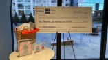 Large printed event check sign mounted on easel with promotional materials on table in Chicago