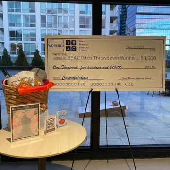 Large printed event check sign mounted on easel with promotional materials on table in Chicago