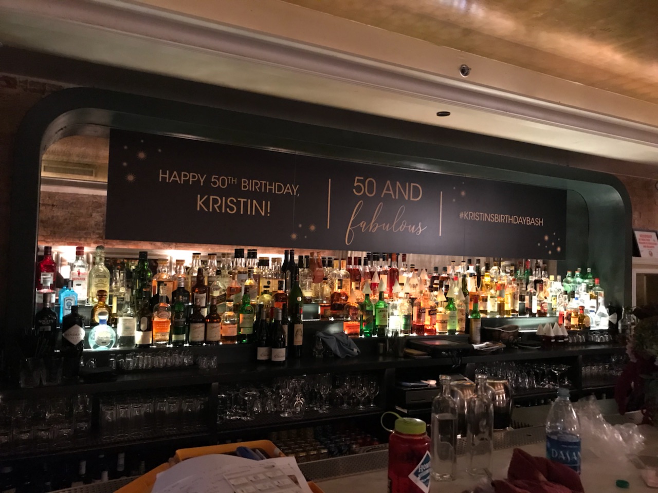 Large printed vinyl banner sign above a bar with liquor bottles in Chicago Downtown.