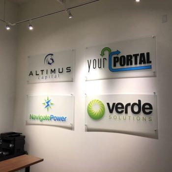 Four rectangular acrylic wall signs with logos mounted on a white wall in Chicago Downtown.