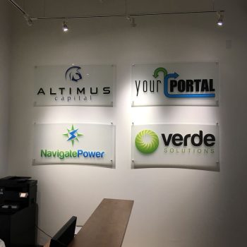 Four rectangular acrylic wall signs with logos mounted on a white wall in Chicago Downtown.