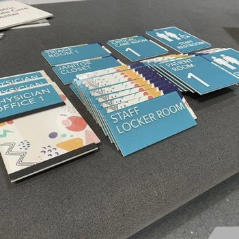 Multiple ADA compliant room and restroom signs made of rigid plastic laid out on a table in Chicago