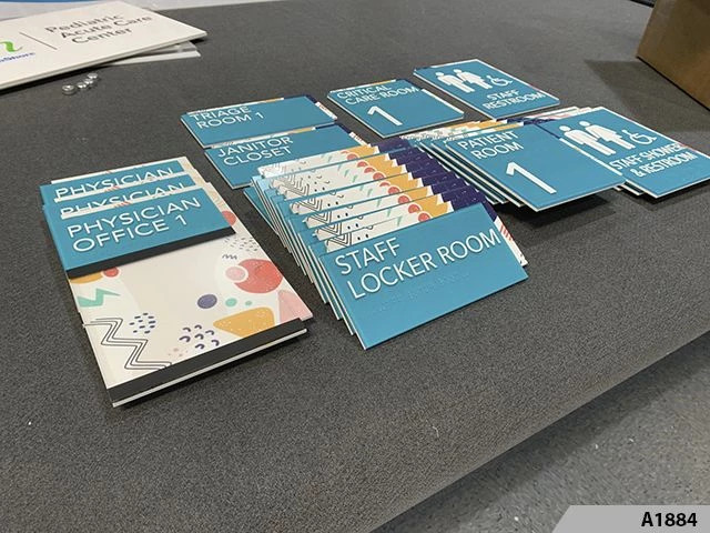 Multiple ADA compliant room and restroom signs made of rigid plastic laid out on a table in Chicago
