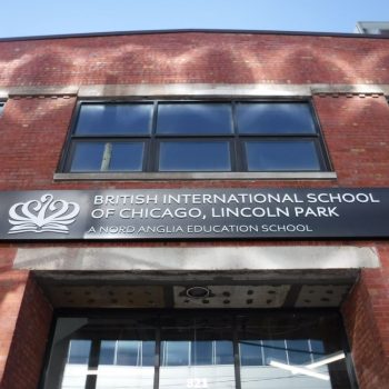 Rectangular black metal storefront sign with raised white letters on brick wall in Chicago Downtown.