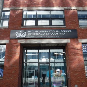 Rectangular metal storefront sign mounted above glass entrance doors on a brick building in Chicago