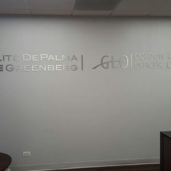 Metal wall sign with brushed silver letters mounted on gray wall in Chicago Downtown office.