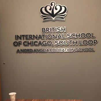 Metal wall sign with layered cutout letters and logo mounted on gray wall in Chicago Downtown.