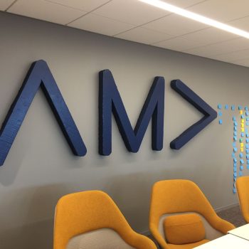 3D wooden office wall signs mounted above orange chairs in a meeting room in Chicago Downtown.