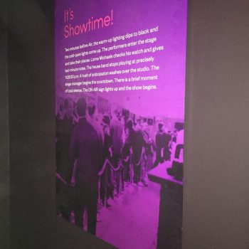 Purple illuminated wall graphic reading “It’s Showtime!” with historical text and a black-and-white crowd photo in an indoor exhibit.