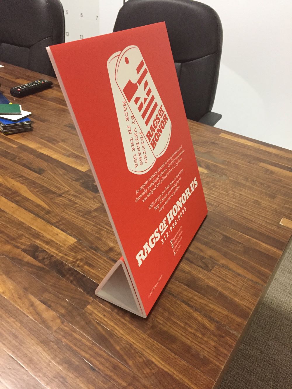 Red tabletop sign with printed branding displayed on a wooden conference table using a folded stand.
