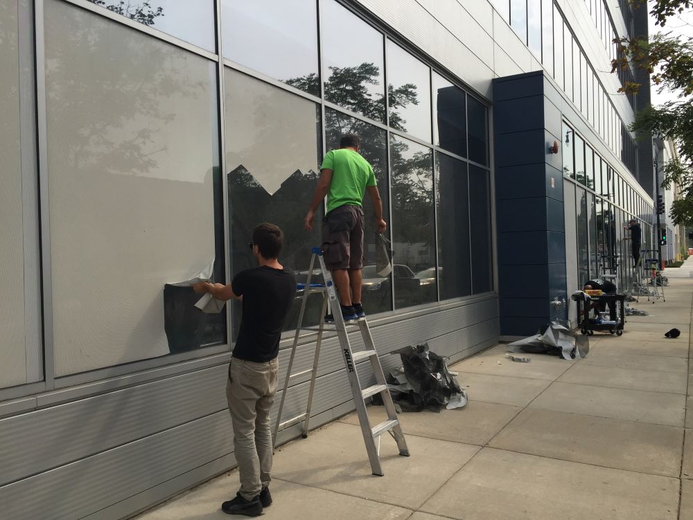 Two workers installing large window vinyl graphics on a commercial building in Chicago Downtown.