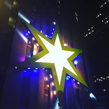 Large illuminated star-shaped wall sign with LED lights on building facade in Chicago Downtown.
