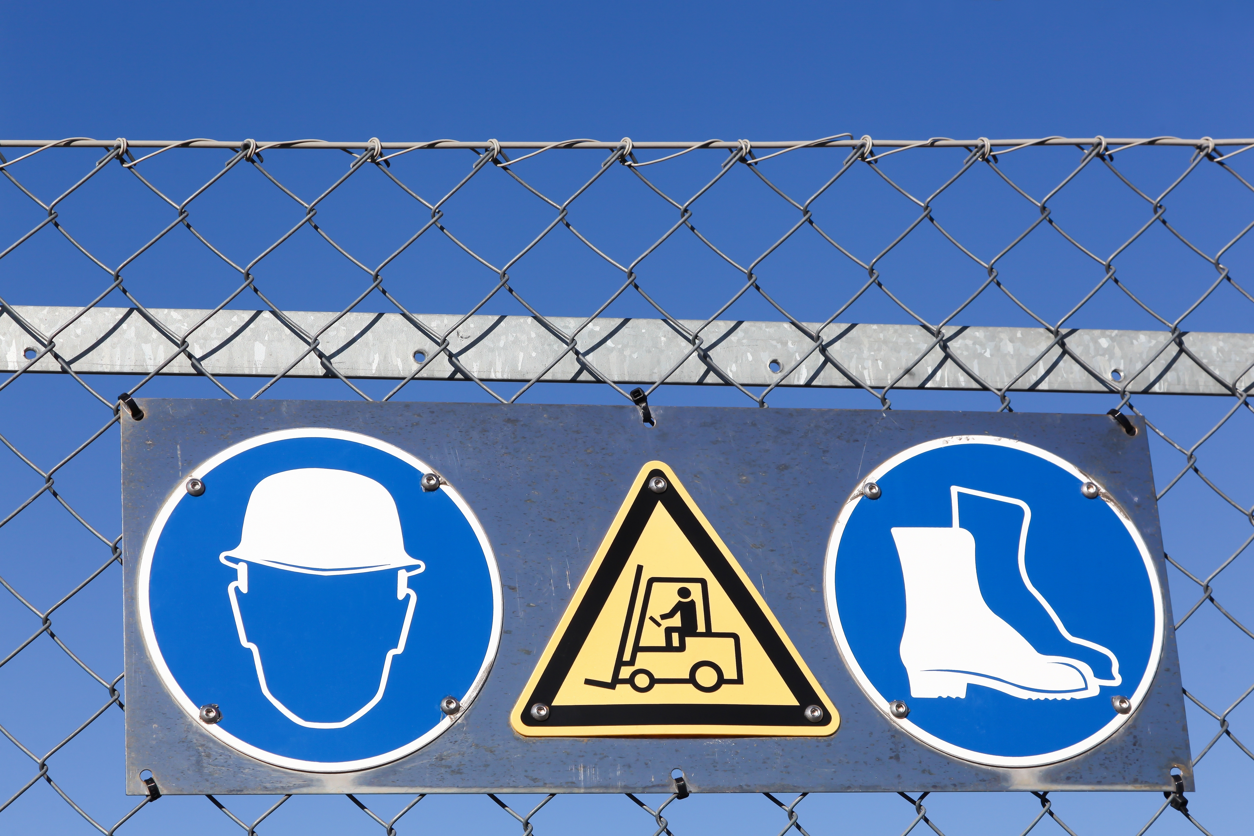 Safety signs on a fence advising reader to wear a hardhat and shoes