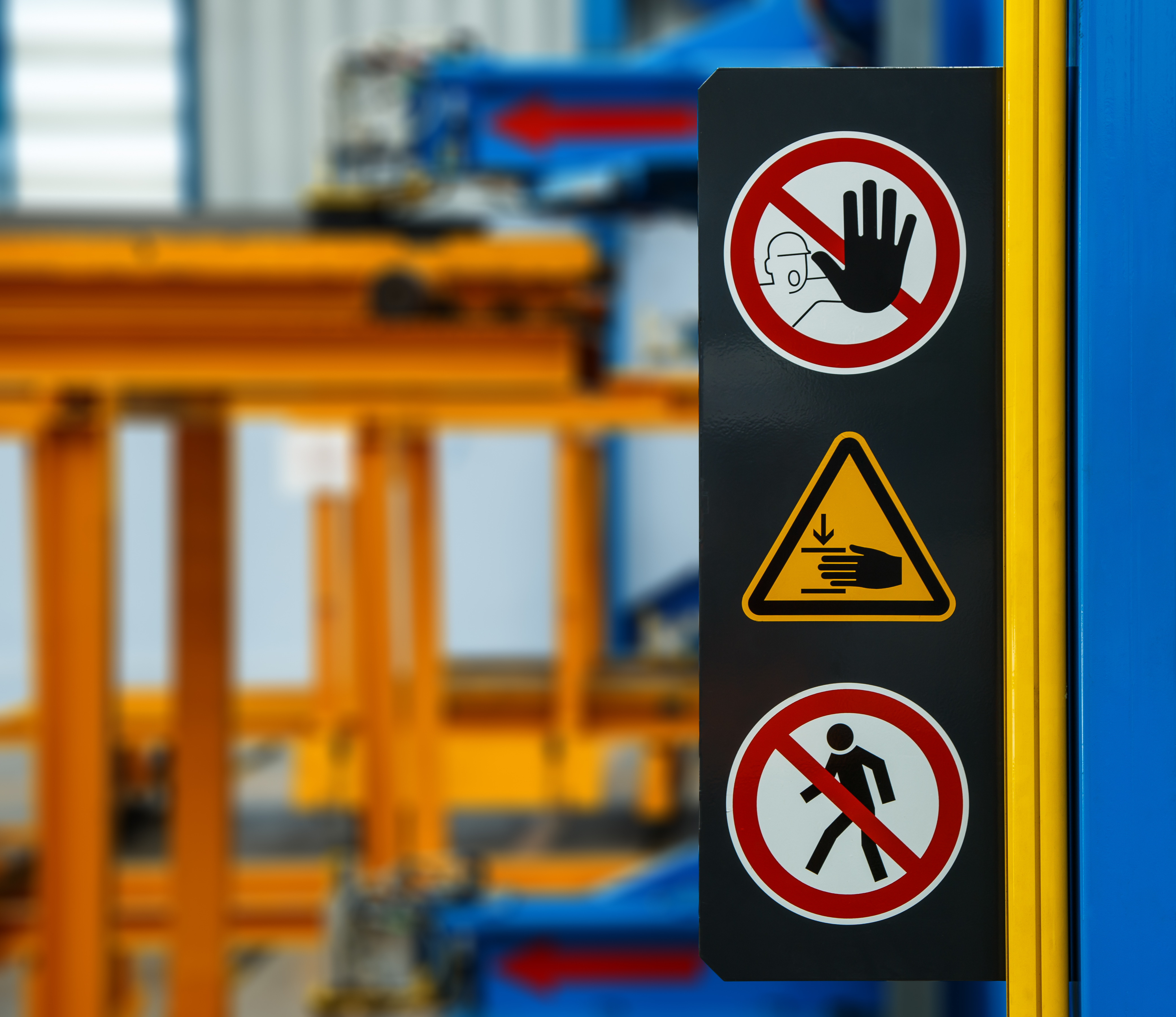 3 saftey signs on a sign in front of machinery 