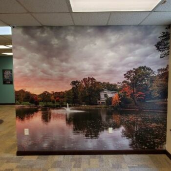 A wall mural depicting a lakeside landscape at sunset. Installed inside an office or public building.