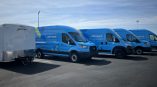 Three blue commercial fleet vans with full vehicle wraps parked beside a white trailer in Dayton,