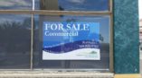 A custom made sign hanging in the window of a commercial property for sale.