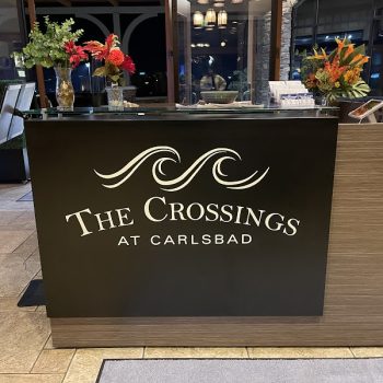 Black vinyl reception desk sign with white lettering and wave design in San Diego, CA.