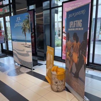 Two retractable banner stands and a small yellow acrylic display with a basket on tiled floor in San