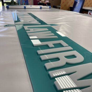Teal acrylic wall sign with raised white lettering on a table in San Diego, CA.