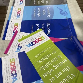 Colorful vinyl banners with grommets laid out on a table in San Diego, CA.
