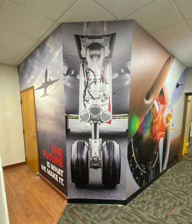 3-wall murall with photos of a plane in the sky, a plane's landing gear and a plane's engine propellor.
