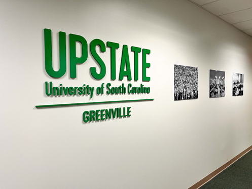 USC Upstate's green dimensional logo in hallway with black and white images next to it.