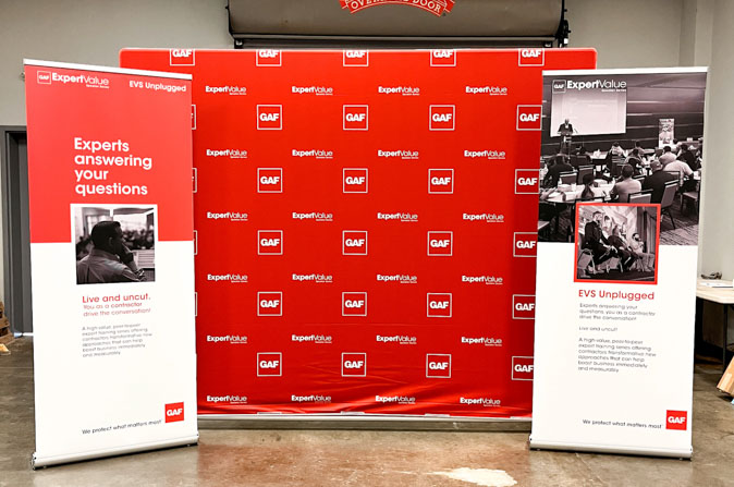 Tradeshow display of red step-and-repeat fabric background and two custom retractables.