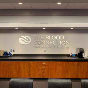 Brushed aluminum dimensional lettering of the Blood Connection logo above conference room bar.