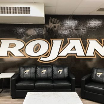 Custom wall mural on cinderblock wall with Trojans written across a brown background.