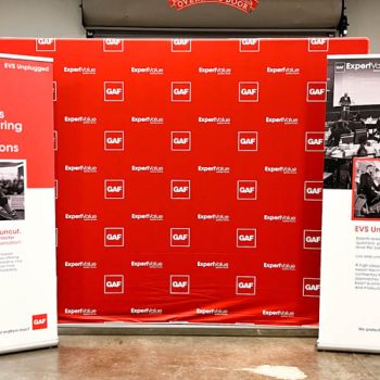 Tradeshow display of red step-and-repeat fabric background and two custom retractables.