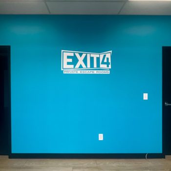 White vinyl logo against painted blue wall at Exit 4