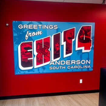 Large wall decal of a blue and red postcard installed on a red wall at Exit 4 in Anderson, SC