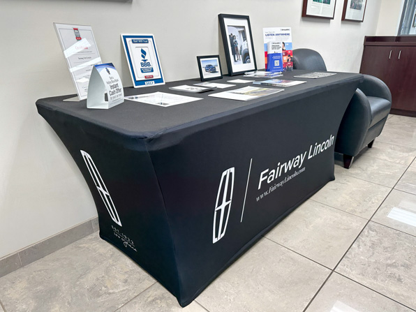Black stretch fabric table throw with white logos in lobby with handouts and awards displayed on top at Fairway Lincoln
