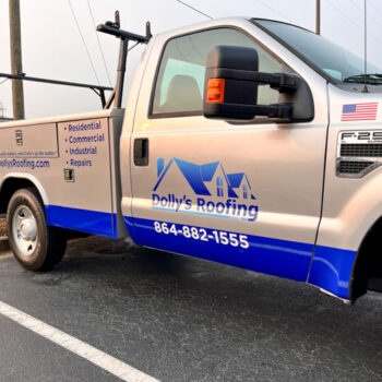 Bright blue logo, contact info and services on a grey service truck for Dolly's Roofing in Greenville, SC