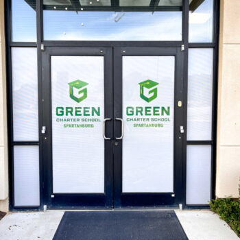 White storefront window perf with green logos at Green Charter School of Spartanburg, SC