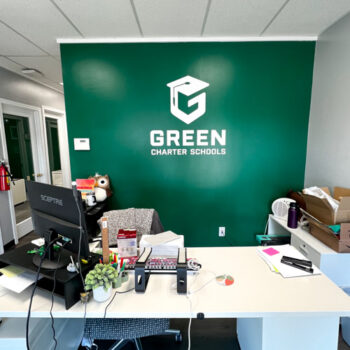 Custom cut decal white logo decal on green wall at Green Charter Schools office in Greenville, SC