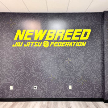 Custom interior wall mural overlaying yellow logo and brand elements on grey topical background for Newbreed in Greenville, SC