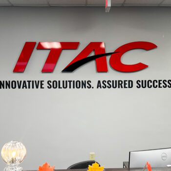 Red and black dimensional logo with tagline in black vinyl installed behind receptionist desk at ITAC in Greenville, SC