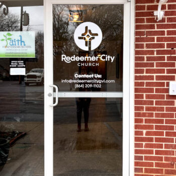 White vinyl decal on glass door featuring logo and contact information for Redeemer City Church in Greenville, SC