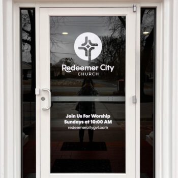 White vinyl decal on glass door featuring logo and service information for Redeemer City Church in Greenville, SC.