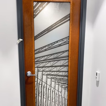 Custom door window display combining a metal beam pattern on clear vinyl and privacy frosting at Trehel in Greenville, SC.