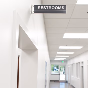 Dark grey acrylic directional sign indicating restrooms with white text for Peterbilt in Columbia, SC