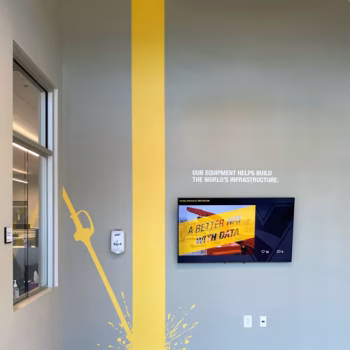 Pipe themed wall decals custom cut from yellow vinyl next to the lobby TV at Vermeer's Piedmont, SC facility.