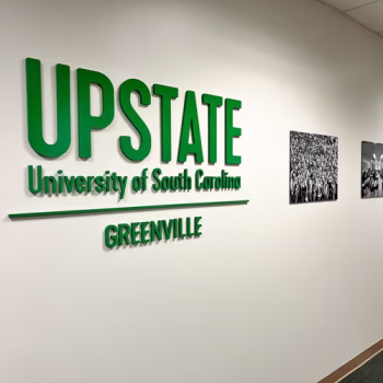 USC Upstate's logo in green dimensional acrylic lettering in hallway next to black and white campus life images at the University Center of Greenville in Greenville, SC.
