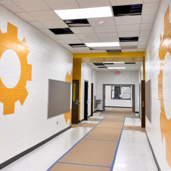 Custom colored yellow vinyl gears installed on a cinderblock wall in a classroom corridor at Wellford Academy.