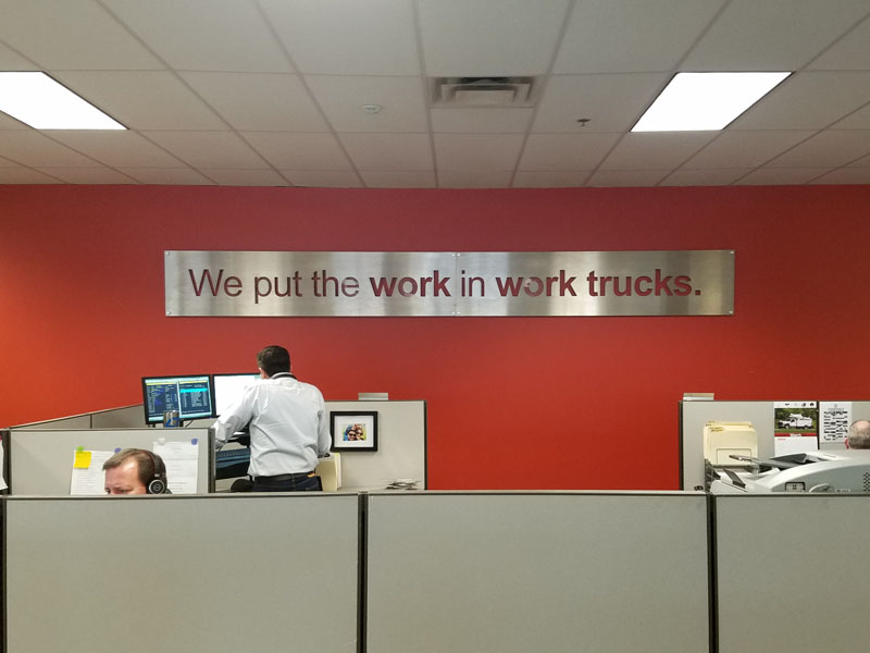 Sign that says we put the work in work trucks hanging up on an indoor office building wall